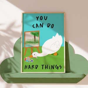 May include: A motivational poster with a white goose painting on a canvas. The goose is holding a paintbrush and is looking at a colorful paint palette. The poster has a blue background and the text "YOU CAN DO HARD THINGS" in black.