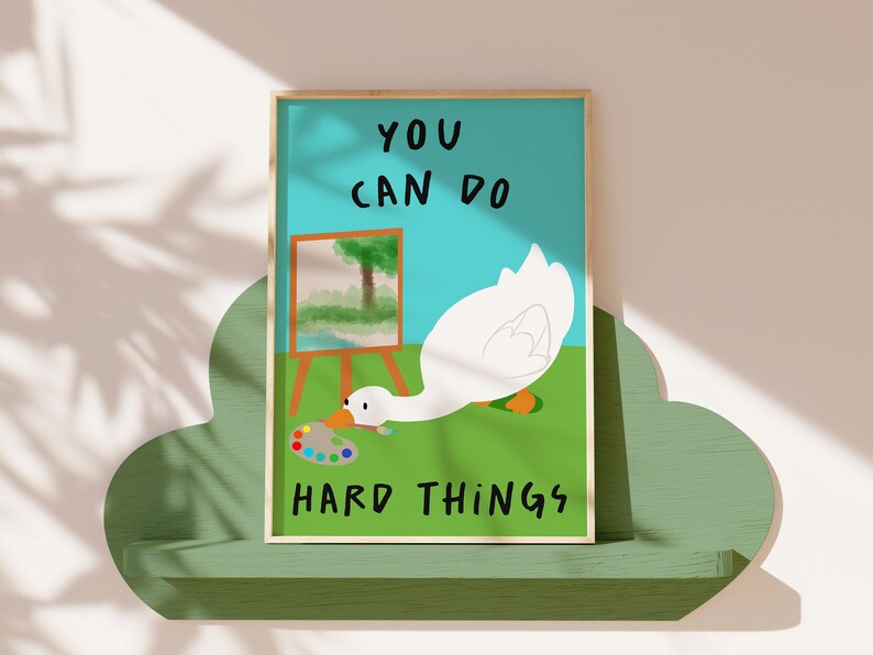 May include: A motivational poster with a white goose painting on a canvas. The goose is holding a paintbrush and is looking at a colorful paint palette. The poster has a blue background and the text "YOU CAN DO HARD THINGS" in black.
