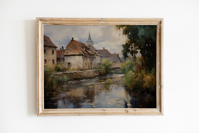 Time-worn village scene artwork in an ornate frame, capturing the rustic beauty of Europe, mounted on a white wall with soft lighting.