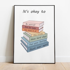 以下が含まれることがあります： 「It's okay to」という黒い文字が書かれた白いポスターと、各本に文字が書かれたカラフルな本の積み重ね。本の文字は、「Be yourself」、「Ask for help」、「Not know it all」、「Make mistakes」、「Have hard days」、「Feel your feelings」、「Start over again」です。