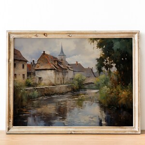 Antique-style painting depicting a quaint village and steeple reflecting in water, displayed on a wooden table against a white wall