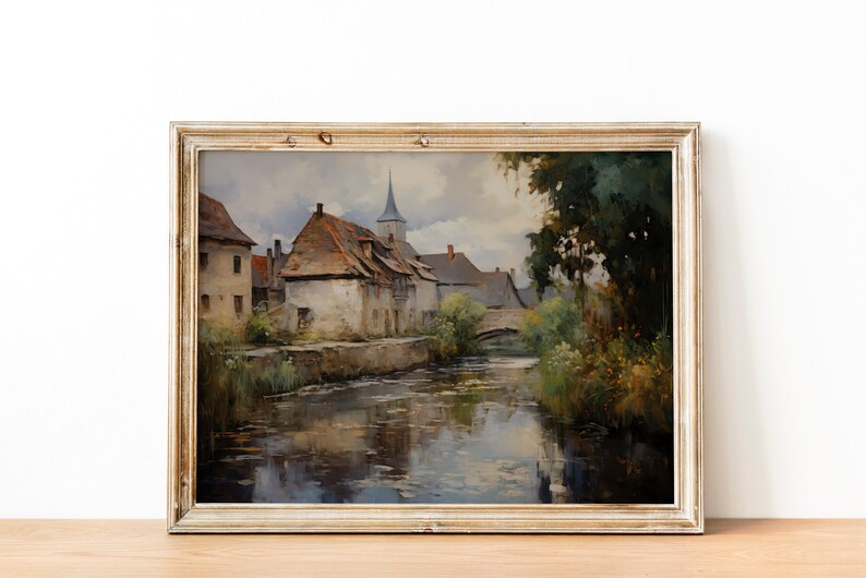Antique-style painting depicting a quaint village and steeple reflecting in water, displayed on a wooden table against a white wall