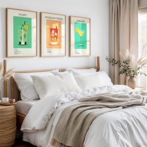 Three framed cocktail prints (Mojito, Malibu Bay Freeze, Margarita) hanging above a cozy bed with white linens, adding a vibrant touch to the bedroom décor.