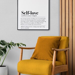 A print highlighting the definition of self-love in bold typography, framed and hung above a comfortable chair, evoking a sense of personal care and positivity.
