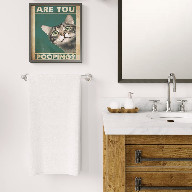 Artistic illustration of a wide-eyed tabby cat on a deep green backdrop, humorously asking 'Are You Pooping?', framed elegantly on a rustic bathroom wall
