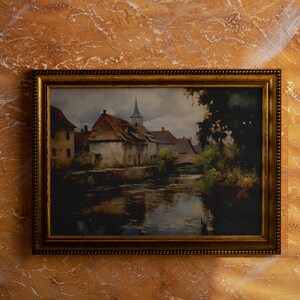 Vintage painting of a rustic European village with reflective river, in a golden frame against a marbled orange wall