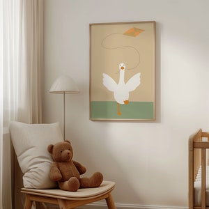 A cozy nursery corner with a framed print of a white goose flying a kite. The print, hung above a beige armchair with a teddy bear, adds a playful yet serene element to the soft-toned room.