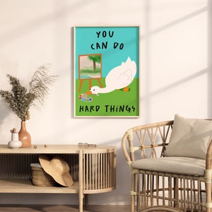 May include: A motivational poster with a white goose painting on a canvas. The goose is looking at a paint palette. The text on the poster reads "You can do hard things."