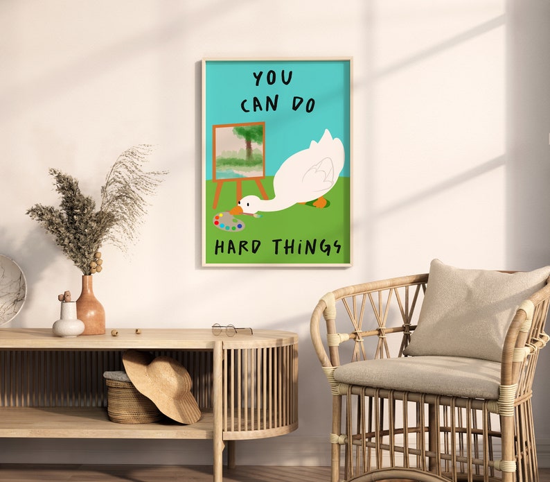 May include: A motivational poster with a white goose painting on a canvas. The goose is looking at a paint palette. The text on the poster reads "You can do hard things."