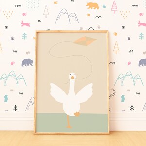 A framed goose nursery print propped against a colorful wallpaper with mountains, trees, and animals. The image of a white goose flying a kite brings a touch of whimsy and adventure to the space.