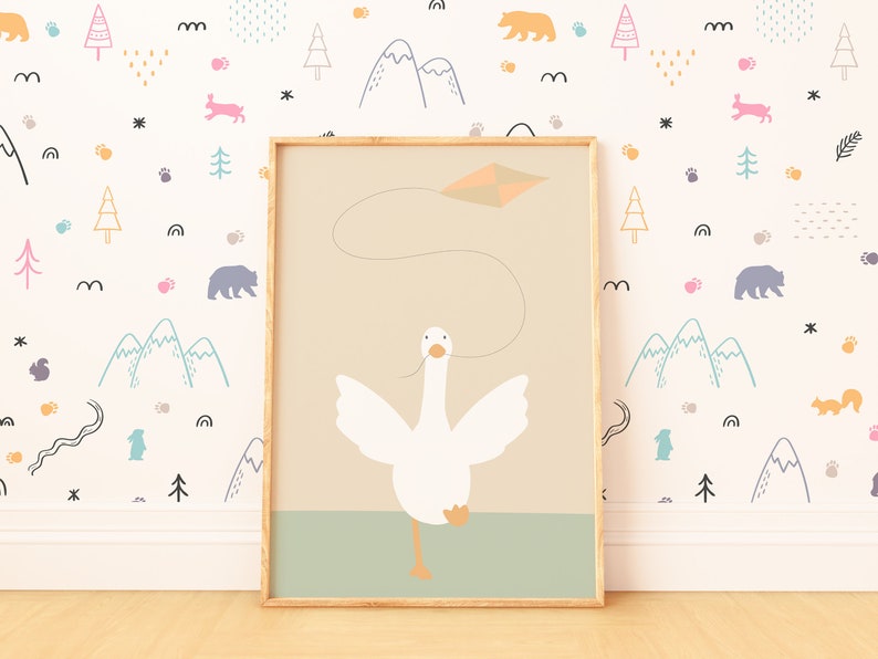A framed goose nursery print propped against a colorful wallpaper with mountains, trees, and animals. The image of a white goose flying a kite brings a touch of whimsy and adventure to the space.