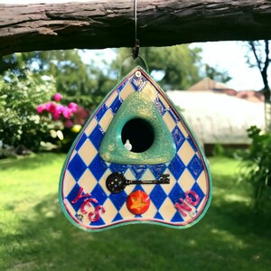 May include: A blue and white triangular birdhouse with a keyhole and the words "YES" and "NO" on the front. The birdhouse is hanging from a branch.