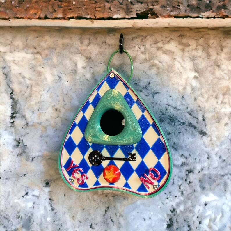 May include: A blue and white triangular shaped wooden birdhouse with a green triangular shaped opening in the front. The birdhouse has the words "YES" and "NO" written on it and a keyhole with a key in it.
