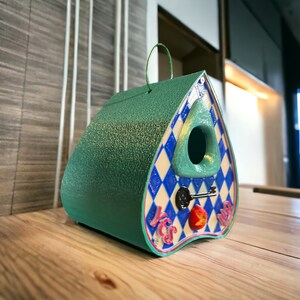 May include: A teal blue birdhouse shaped like a witch's hat with a diamond pattern and the words "Yes" and "No" on the front. The birdhouse has a small opening for birds to enter and a keyhole with a key.