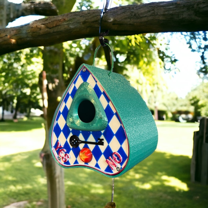 May include: A teal blue birdhouse shaped like a heart with a white and blue diamond pattern. The birdhouse has a small opening for birds to enter and a keyhole with a key. The words "Yes" and "No" are written on the bottom of the birdhouse.