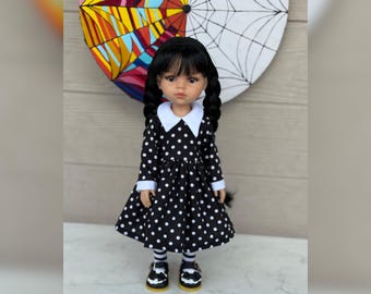 May include: A doll in a black polka dot dress with a white collar and cuffs, black pigtails, and black shoes with white details. The background features a colourful, abstract design and a spiderweb.