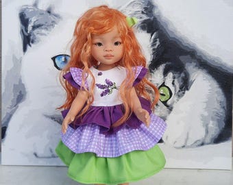 May include: A doll with red hair and a white top with a purple floral design. The doll wears a purple and gingham skirt, a green skirt, and green shoes. A painting of a cat's face is in the background.