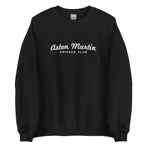 Puede incluir: Sudadera negra con un estampado gráfico blanco que dice "Aston Martin Drivers Club" en una fuente cursiva.