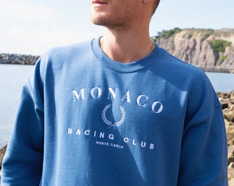 May include: A blue sweatshirt with a white embroidered logo that says "MONACO RACING CLUB MONTE CARLO"