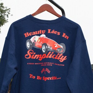 Puede incluir: Sudadera de manga larga azul marino con un gráfico rojo de un coche de carreras vintage y el texto "Beauty Lies In Simplicity. A front-mounted naturally aspirated inline-four. To Be Specific..."