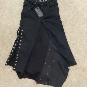 Peut inclure: Jupe en jean noire avec un détail de laçage sur le côté et un ourlet brut. La jupe porte une étiquette de taille indiquant "Taille 1-6, Max 18F, 10,00 €".