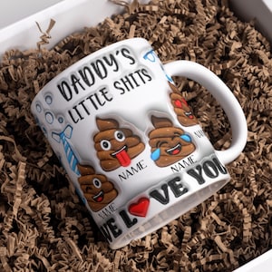 K&ouml;nnte beinhalten: Wei&szlig;e Keramiktasse mit dem Text "Daddy's Little Shits" und einem Herz mit dem Text "We Love You". Die Tasse ist mit Kack-Emojis mit verschiedenen Gesichtsausdr&uuml;cken verziert.