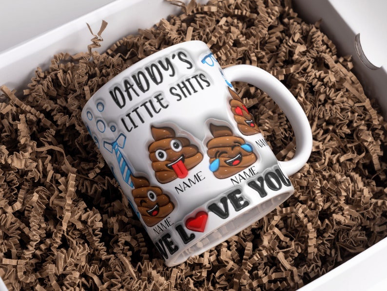 K&ouml;nnte beinhalten: Wei&szlig;e Keramiktasse mit dem Text "Daddy's Little Shits" und einem Herz mit dem Text "We Love You". Die Tasse ist mit Kack-Emojis mit verschiedenen Gesichtsausdr&uuml;cken verziert.