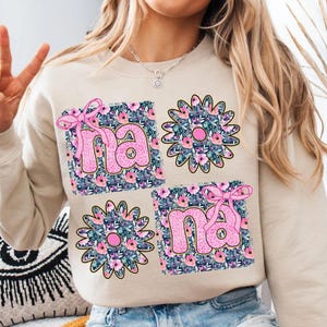 May include: A beige sweatshirt with a floral design and the word "nana" printed in pink letters.