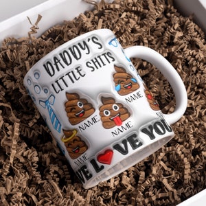 K&ouml;nnte beinhalten: Eine wei&szlig;e Keramiktasse mit dem Text "Daddy's Little Shits" und einem roten Herzen. Die Tasse hat eine blaue Krawatte und mehrere Kack-Emojis mit verschiedenen Gesichtsausdr&uuml;cken. Der Text "We Love You" ist um den Boden der Tasse geschrieben.
