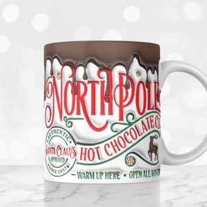 May include: White ceramic mug with a brown chocolate-like glaze dripping down the side. The mug features the text "North Pole Hot Chocolate Co." with a reindeer illustration and the words "Authentic Santa Claus Approved Since 1897" in a circle. The text "Warm Up Here - Open All Winter" is printed below the main text.