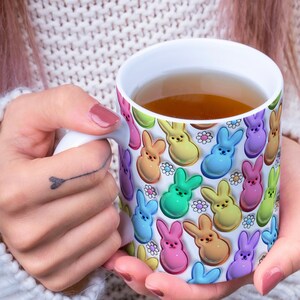 May include: A white ceramic mug with a colorful pattern of pastel-colored bunny shapes and white daisies. The mug is filled with a light brown liquid.