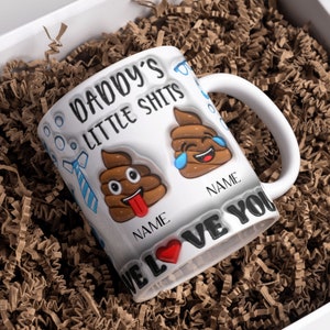 K&ouml;nnte beinhalten: Wei&szlig;e Keramiktasse mit einem schwarzen und braunen Design. Die Tasse tr&auml;gt den Text "Daddy's Little Shits" und zwei Kack-Emojis. Der Text "We Love You" befindet sich am Boden der Tasse.