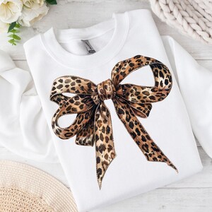 May include: White sweatshirt with a large leopard print bow on the front.
