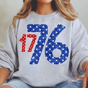 May include: A gray sweatshirt with a red and blue glitter design of the number 1776. The numbers are made up of white stars on a blue background.