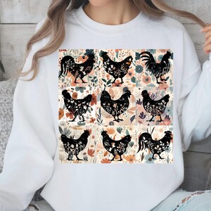 May include: White sweatshirt featuring a colorful floral and chicken design. The design includes nine black chicken silhouettes filled with floral patterns, set against a backdrop of flowers in various colors.
