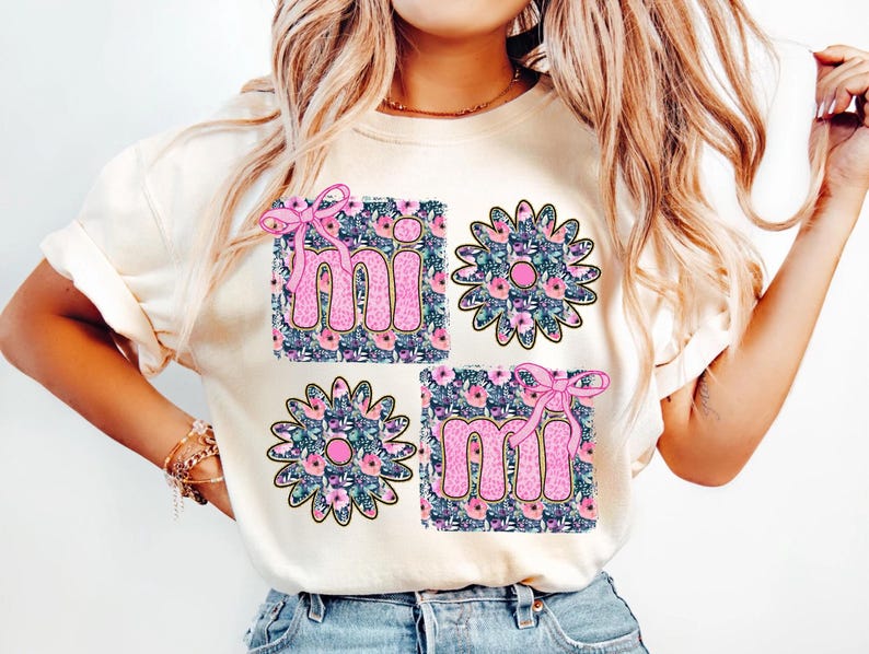 May include: A white t-shirt with a floral design and the word "mi" repeated twice. The floral design is in shades of pink, blue, and green.