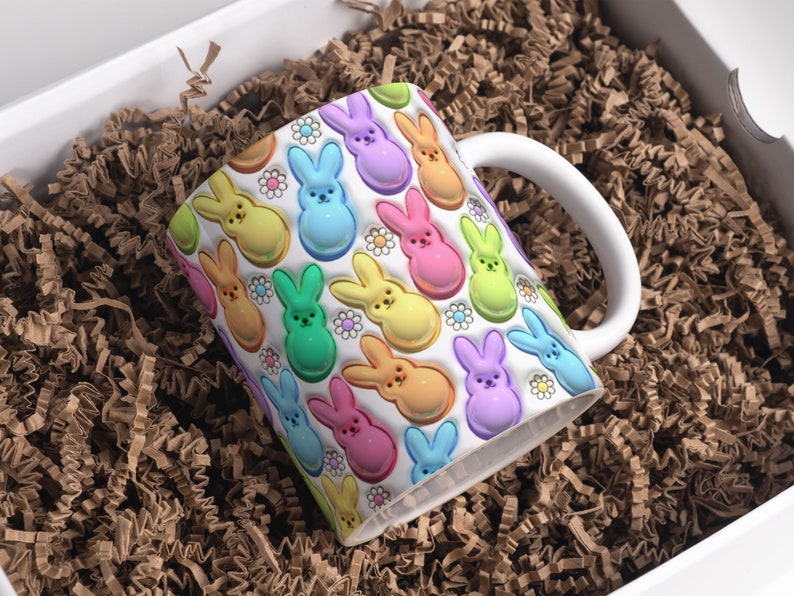 May include: A white ceramic mug with a colorful pattern of pastel-colored bunny-shaped candies. The mug has a white handle and is filled with brown packing peanuts.