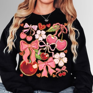 May include: Black sweatshirt with a colorful print of cherries, bows, and flowers. The print is in shades of pink, red, and green.