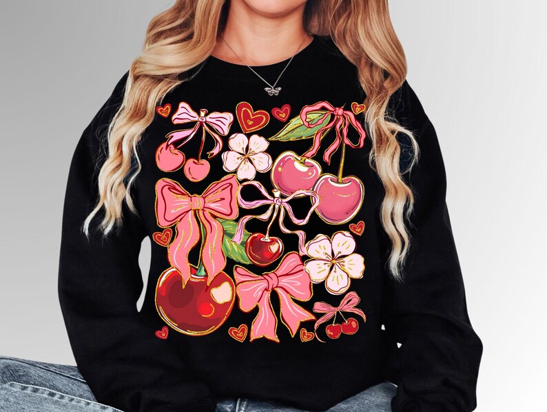 May include: Black sweatshirt with a colorful print of cherries, bows, and flowers. The print is in shades of pink, red, and green.