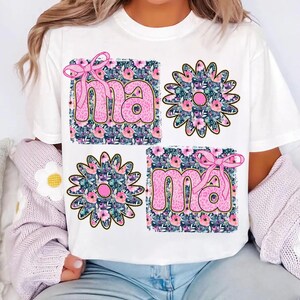 May include: White t-shirt with a pink and gold floral design and the word "mama" printed twice in pink letters.