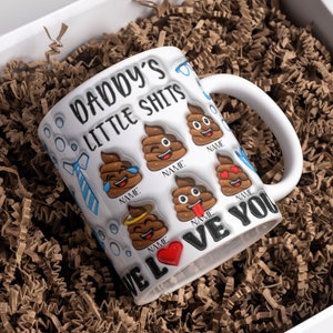 K&ouml;nnte beinhalten: Wei&szlig;e Keramiktasse mit einem lustigen Spruch "Daddy's Little Shits" und Kack-Emoji-Grafiken. Die Tasse hat ein rotes Herz und die Worte "We Love You".