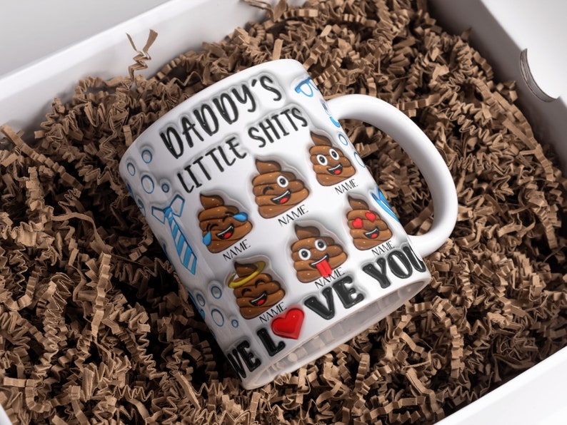K&ouml;nnte beinhalten: Wei&szlig;e Keramiktasse mit einem lustigen Spruch "Daddy's Little Shits" und Kack-Emoji-Grafiken. Die Tasse hat ein rotes Herz und die Worte "We Love You".