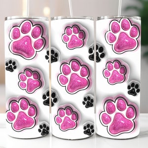 Op de afbeelding: Drie witte roestvrijstalen bekers met roze glitter-pootafdrukken op een witte achtergrond. De bekers hebben zwarte deksels en rietjes.