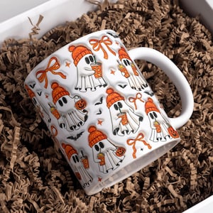 May include: White ceramic mug with a Halloween ghost pattern. The ghosts wear orange beanies and hold drinks and jack-o'-lanterns. The mug is in a white box filled with brown crinkle paper.