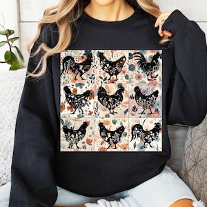 May include: Black sweatshirt featuring a nine-panel design with black rooster and hen silhouettes. Each panel has a floral background in shades of pink, orange, and green. The sweatshirt is a solid black color.