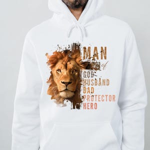 Może przedstawiać: Biała bluza z kapturem z grafiką lwa i tekstem "Man of God, Husband, Dad, Protector, Hero".