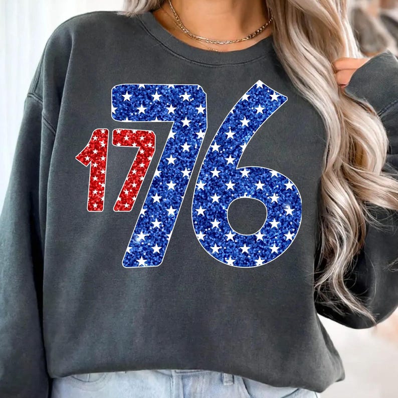 May include: A dark gray sweatshirt with a red and blue glitter design of the number 1776. The numbers are made up of white stars.