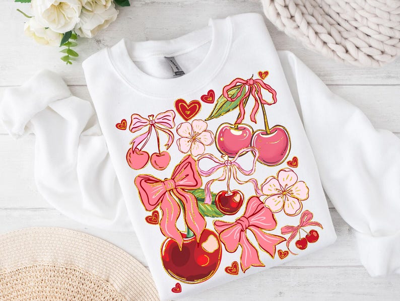 May include: White sweatshirt with a pink and red cherry design. The cherries have pink bows and are surrounded by pink flowers and hearts.