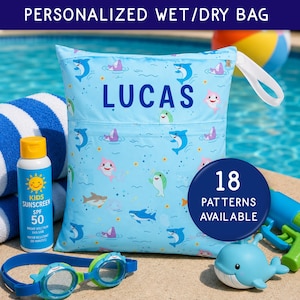 May include: A light blue personalized wet/dry bag with the name "LUCAS" in large blue letters. The bag features a pattern of cartoon sharks and is surrounded by other beach and pool accessories, including sunscreen and goggles.