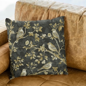 May include: A brown leather couch with a throw pillow featuring a dark gray background with a pattern of gold branches and birds.